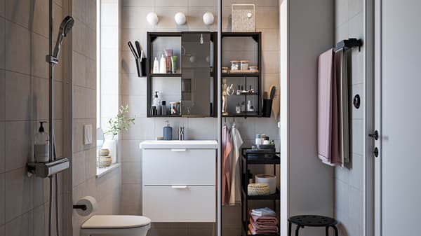 Baño con muebles en blanco y negro, juego de ducha cromado, toallas en rosa claro y una puerta de ducha de cristal.