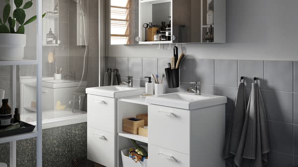 Baño gris con muebles de lavabo en blanco, un armario con puertas de espejo y accesorios de bambú.