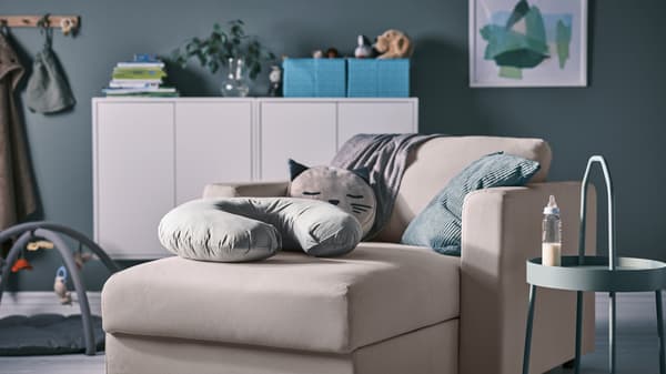 Bantal susuan LEN berwarna kelabu terletak di atas chaise longue VIMLE berwarna kuning air, di sebelah meja sisi BURVIK berwarna kelabu-hijau muda yang mempunyai botol susu.