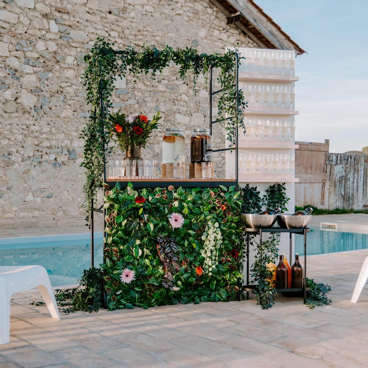 Bar extérieur décoré de plantes vertes et de fleurs avec différentes boissons et verres.