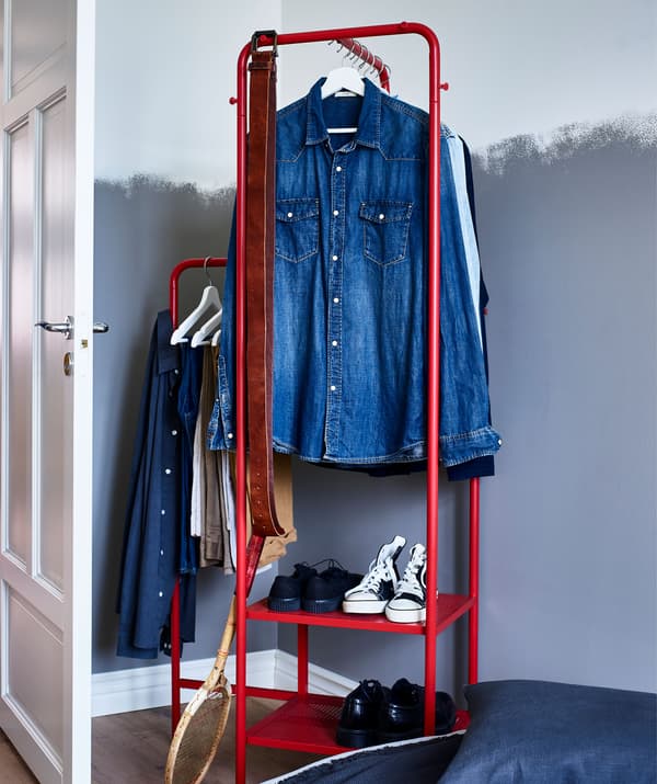Barra para roupa de metal vermello de diferentes alturas con camisas e zapateiro nunha parede pintada.