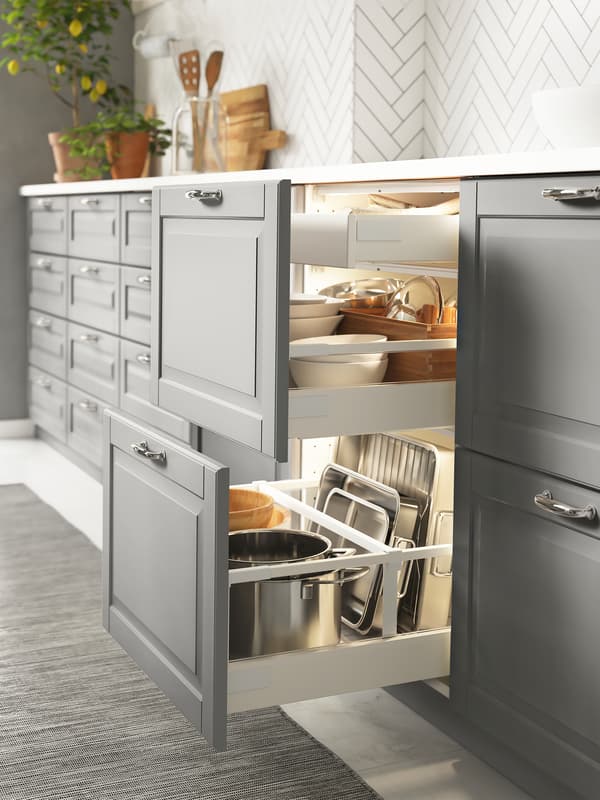 Base cabinets in a kitchen setting with grey drawer fronts, two drawers are open and have cookware and tableware inside.