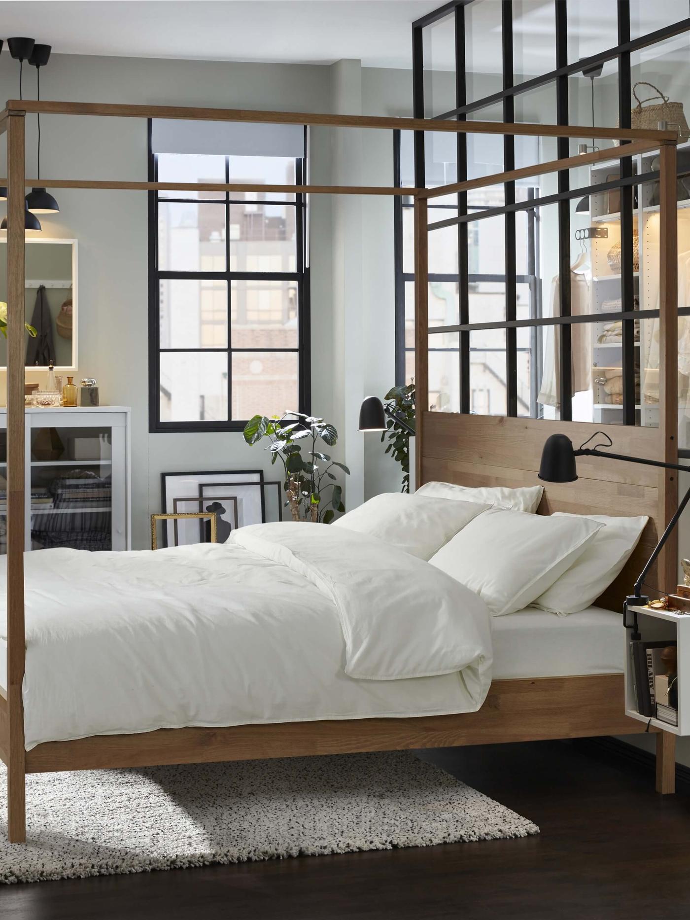 Base de cama con cuatro postes de color café grisáceo en el medio de un dormitorio con ropa de cama blanca.