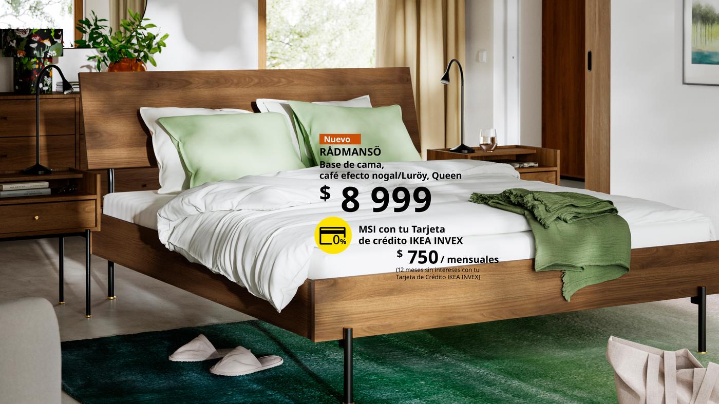 Base de cama RÅDMANSÖ de madera en efecto nogal con cabecera, vestida con ropa de cama blanca y verde, colocada en un dormitorio.