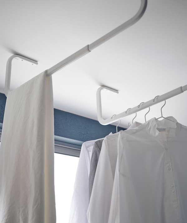 Bastoni appendiabiti MULIG fissati al soffitto di una veranda, con file di panni stesi ad asciugare.
