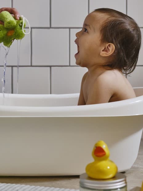 Bath and change
Toddler sitting in a white bathtub, happily reaching out to grab a green bath toy.