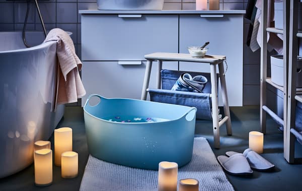 Bathroom mood-lit by scattered LED block candles; a stool placed next to a big footbath, flowers floating in it.
