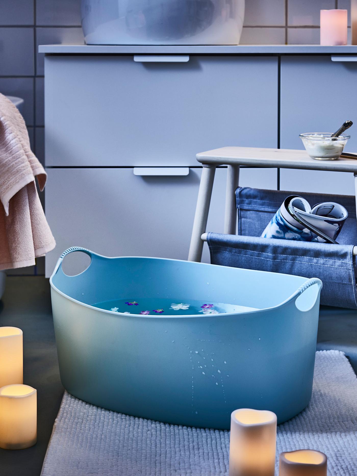 Bathroom mood-lit by scattered LED block candles; a stool placed next to a big foot bath, flowers floating in it.