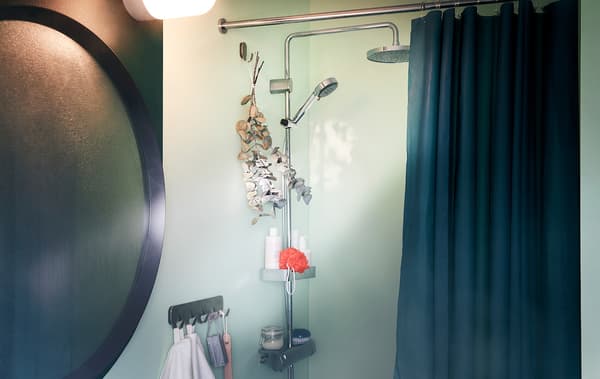 Bathroom with a fogged-up mirror next to a shower with accessories and a bundle of eucalyptus twigs is hung on a hook.