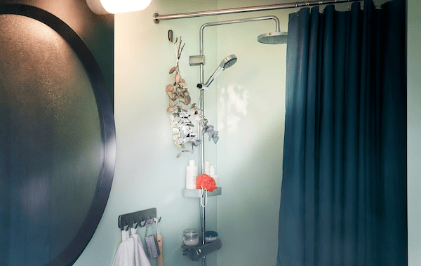 Bathroom with a fogged-up mirror next to a shower with accessories and a bundle of eucalyptus twigs is hung on a hook.