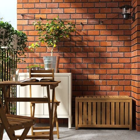 Baúl de madera cerrado pegado a la pared. Hay una mesa y silla de madera plegable y un muble con un macetero y planta encima.