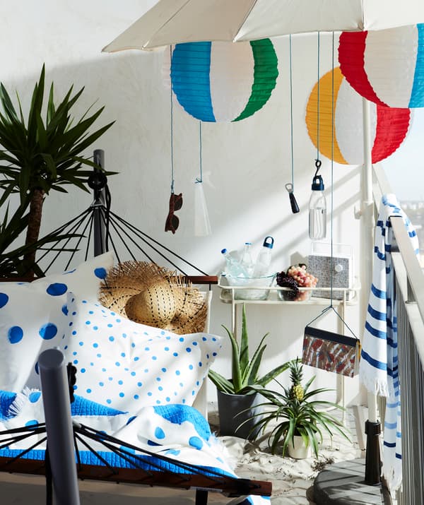 Beach-inspired balcony with hammock and stand, and a parasol with everything from sunglasses to LED lamps hung from it.