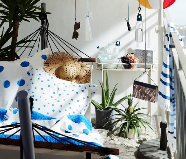 Beach-inspired balcony with hammock and stand, and a parasol with everything from sunglasses to LED lamps hung from it.