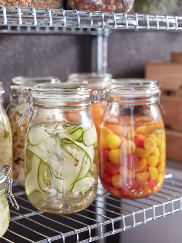 Beberapa balang kaca berpenutup KORKEN berisi pelbagai jenis sayur-sayuran jeruk yang berwarna-warni, terletak di atas para logam.