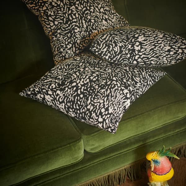 Beberapa sarung kusyen GRIMHILD yang menampilkan corak abstrak berwarna hitam dan semula jadi terletak di atas sofa baldu berwarna hijau.