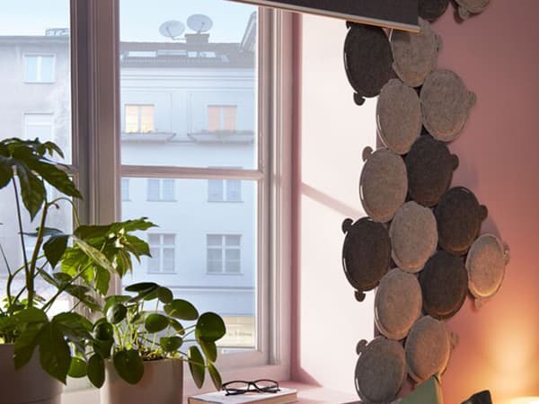 Bed by a window equipped with a black-out roller blind and framed by multiple small, round sound-absorbing panels.