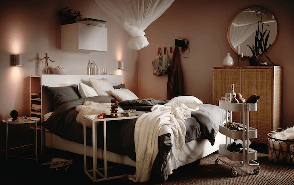 Bed laden with fluffy bedding, cushions and throws, trolley with snacks and drink beside it, a net in a knot hanging above.
