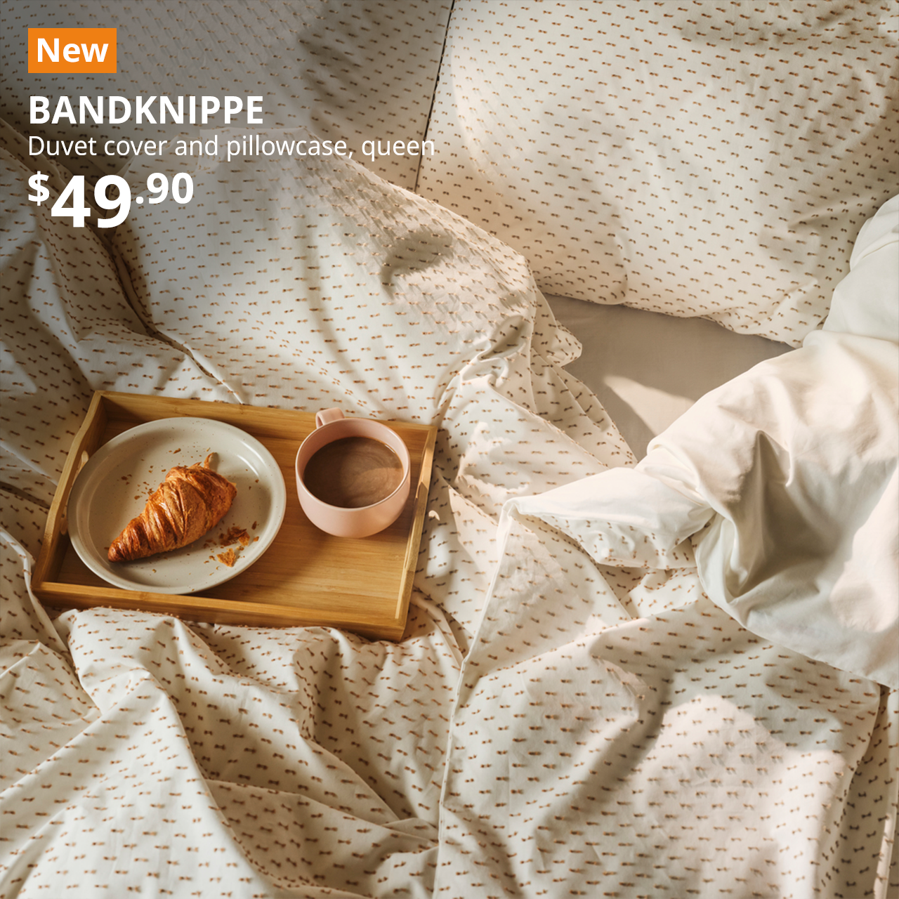 Bed with BANDKNIPPe duvet covers and pillowcases on top, also showing a tray with breakfast laid on top.