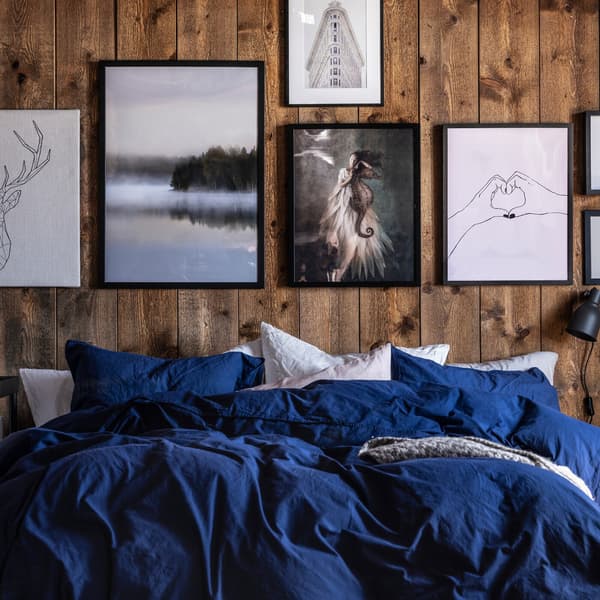 Bed with blue and white bedding and rustic wooden wall decorated with artworks in black, white and grey tints.