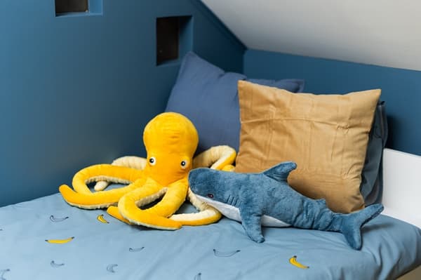 Bed with cushions, featuring a large yellow octopus soft toy in a children’s bedroom.