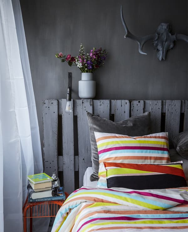 Bed with multi-coloured bedding against grey background decor.
