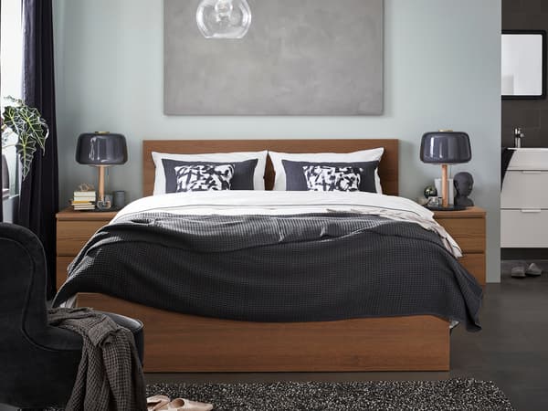 木製ベッドに黒とグレーの寝具を合わせた落ち着いた寝室。モノトーンのランプでモダンな印象。