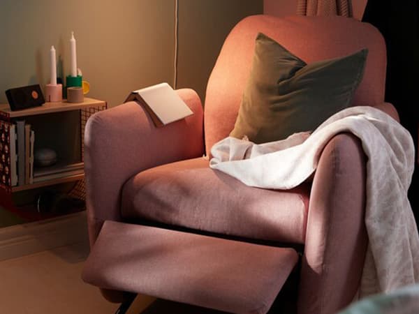 Bedroom corner between bed and a room divider with a recliner, wall-mounted reading light and a small wall shelf.