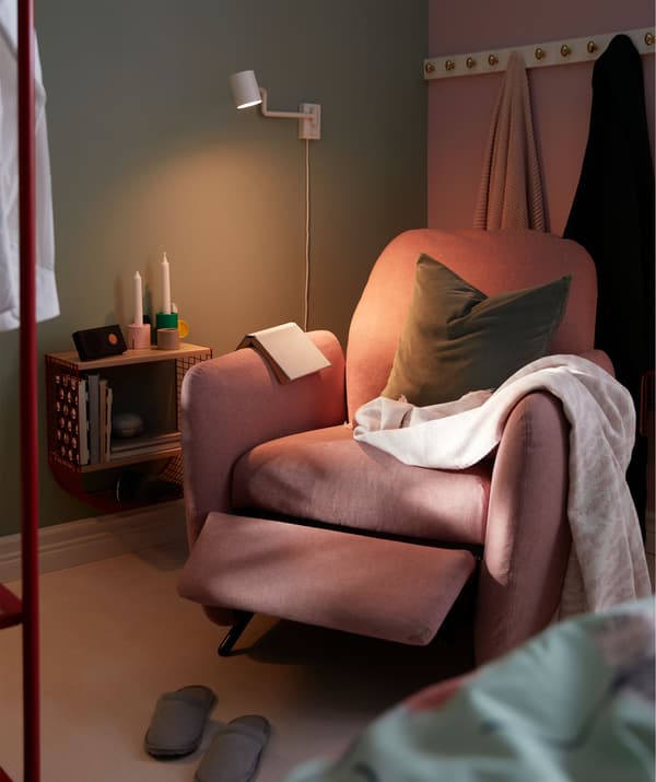 Bedroom corner with a recliner, wall-mounted reading light and a small wall shelf.