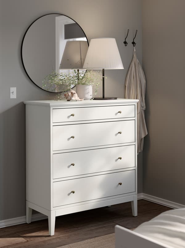Bedroom corner with a white IDANÄS chest of drawers, a lamp and a plant on top of it, a round mirror on the wall above.