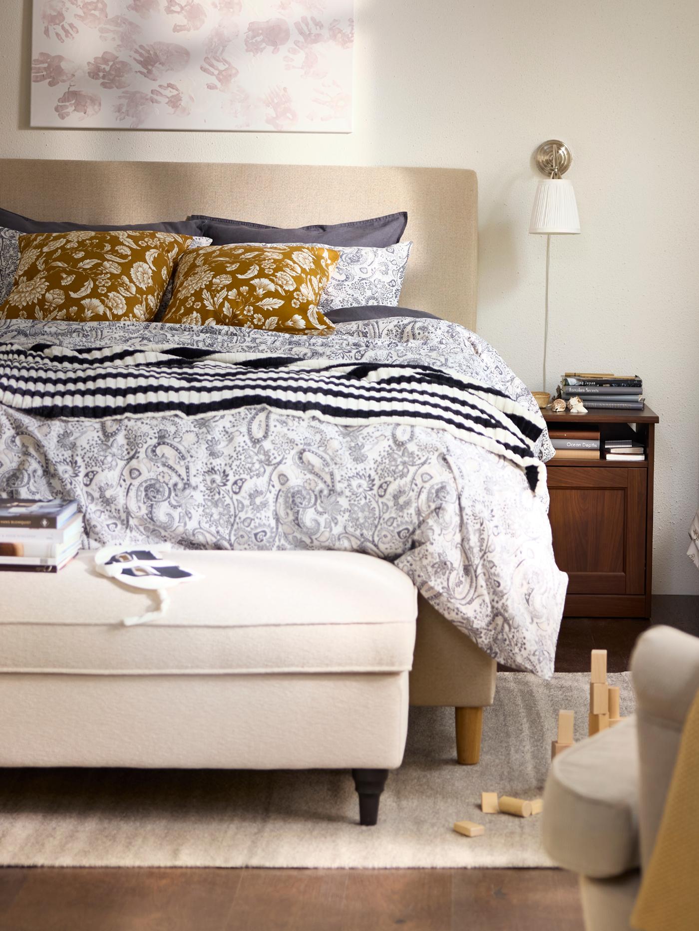 Bedroom in beige and white with a children’s bed next to the grown-up’s bed, and an armchair in the foreground.