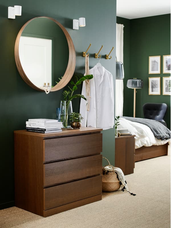 Bedroom with a chest of drawers in black brown veneer, a round mirror, a seagrass basket and hooks.