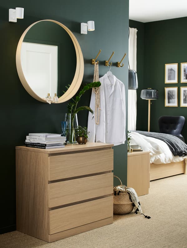 Bedroom with a chest of drawers in white stained oak veneer, a round mirror, a seagrass basket and hooks.