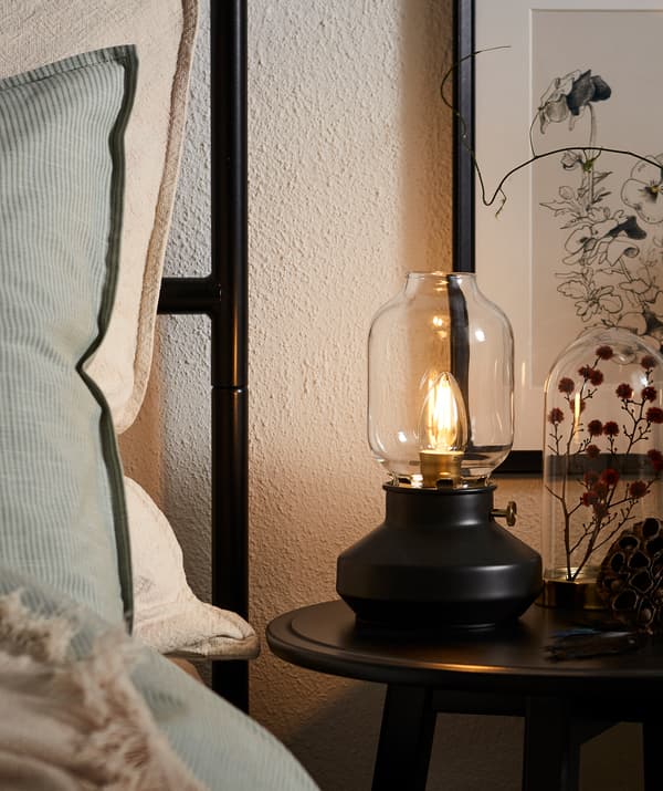 Bedside table with a lit TÄRNABY LED lamp in the form of a kerosene lamp.