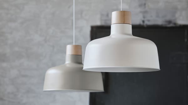 Beige and white BUNKEFLO pendant lamps hang at different heights from a ceiling in an industrial style space.