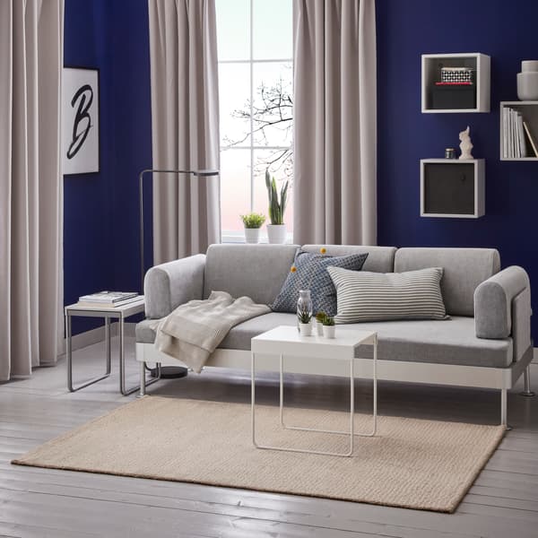 Beige, laagpolig vloerkleed in een woonkamer met een bank en een bijzettafel erop.