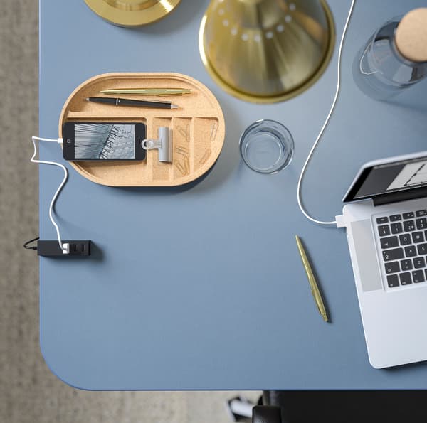BEKANT blauwe tafel van bovenaf met een laptop, een telefoon en bureauaccessoires.