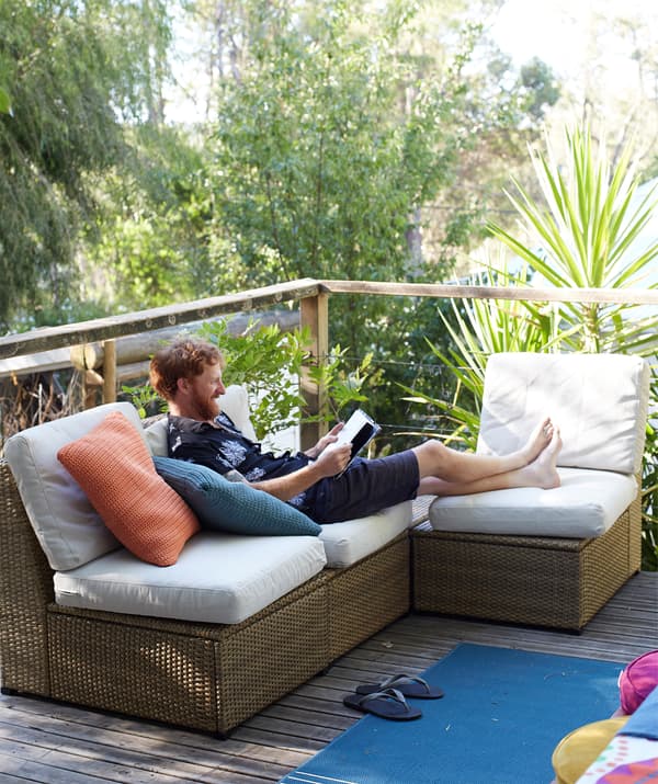 Ben se détend sur un canapé d’angle d’extérieur placé sur une terrasse surélevée dans le jardin.