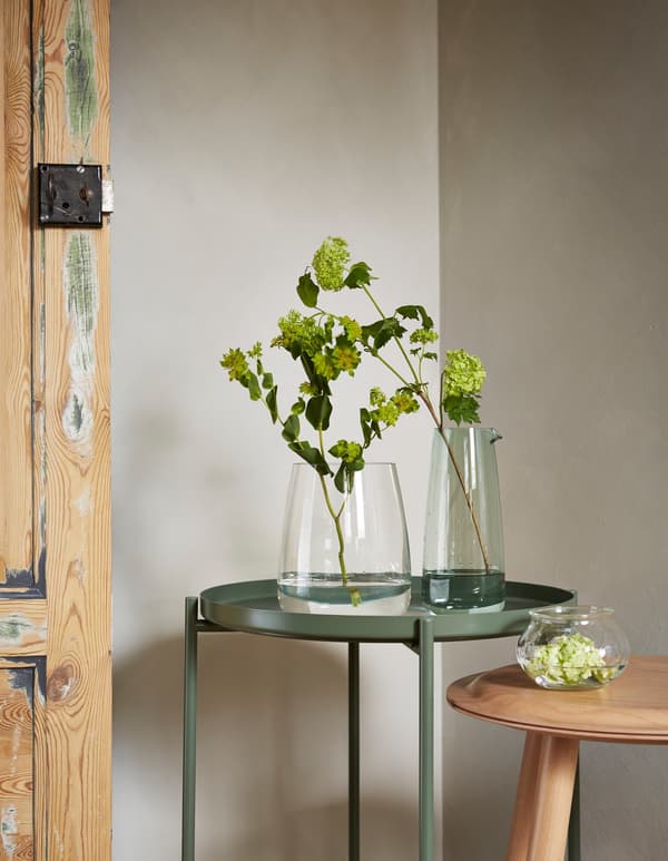BERÄKNA and VILJESTARK vases on a table, with a single plant and a green budding branch showing that simple things can be beautiful.