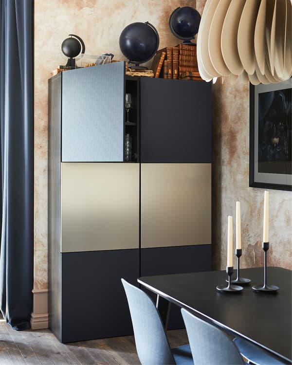 BESTÅ تشكيلة تخزين بلون أسود-بني مع أبواب زرقاء، خلف طاولة طعام عليها شمعدانات وبعض الكراسي.