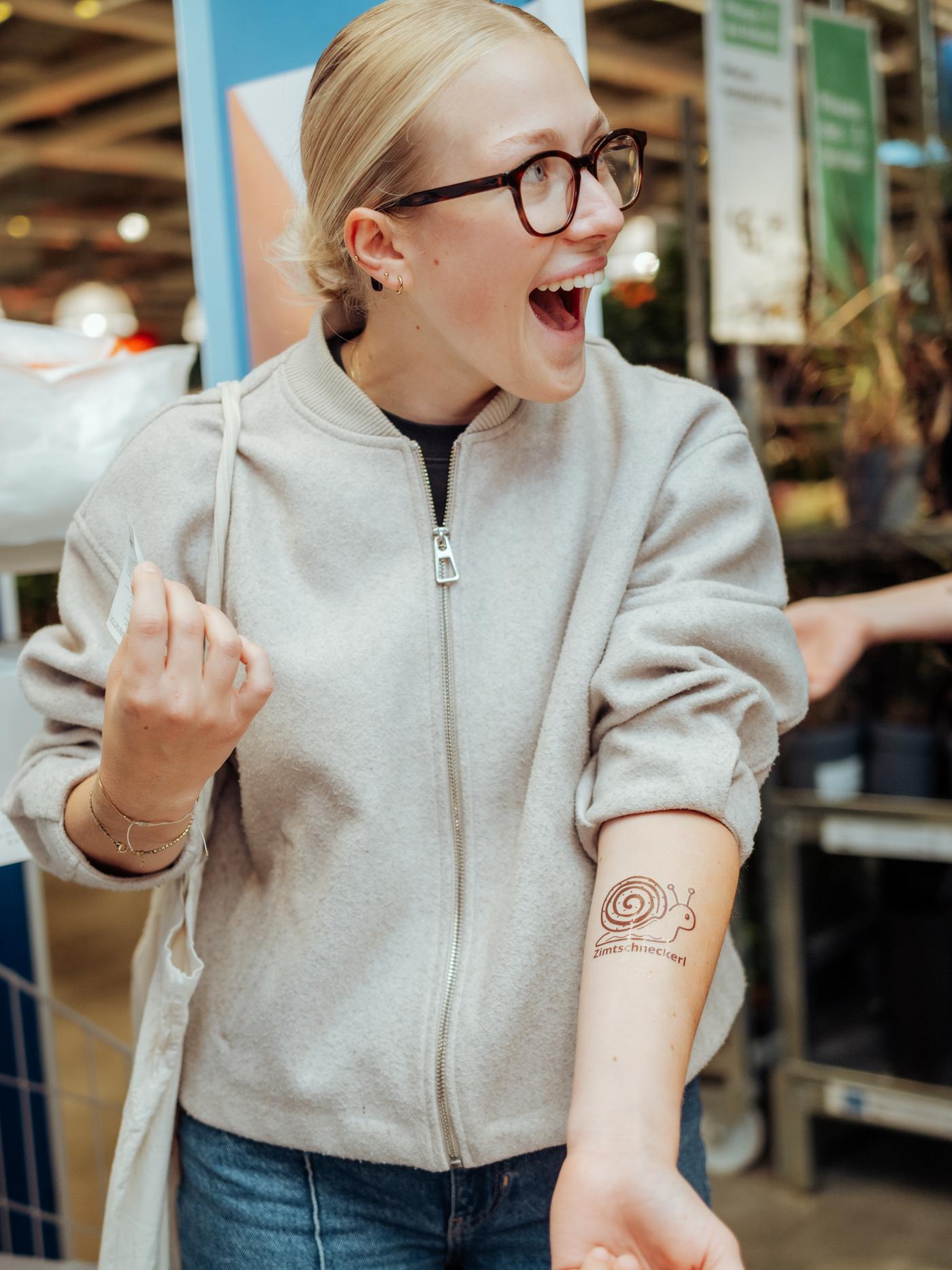Besucherin freut sich über ein temporäres Zimtschnecken-Tattoo auf ihrem Unterarm.