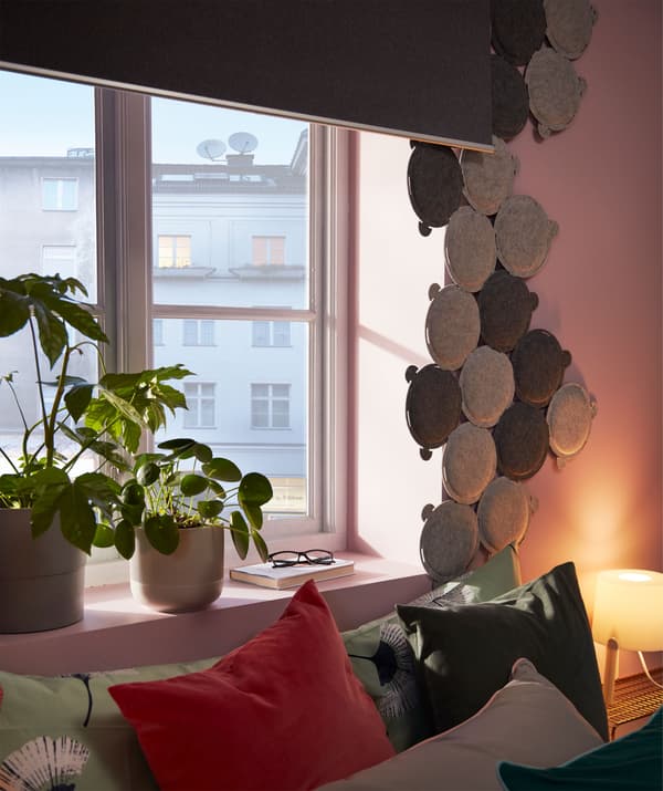 Bett an einem Fenster mit Verdunklungsrollo und einem Behang aus einigen ODDLAUG Paneelen, die Geräusche dämmen.