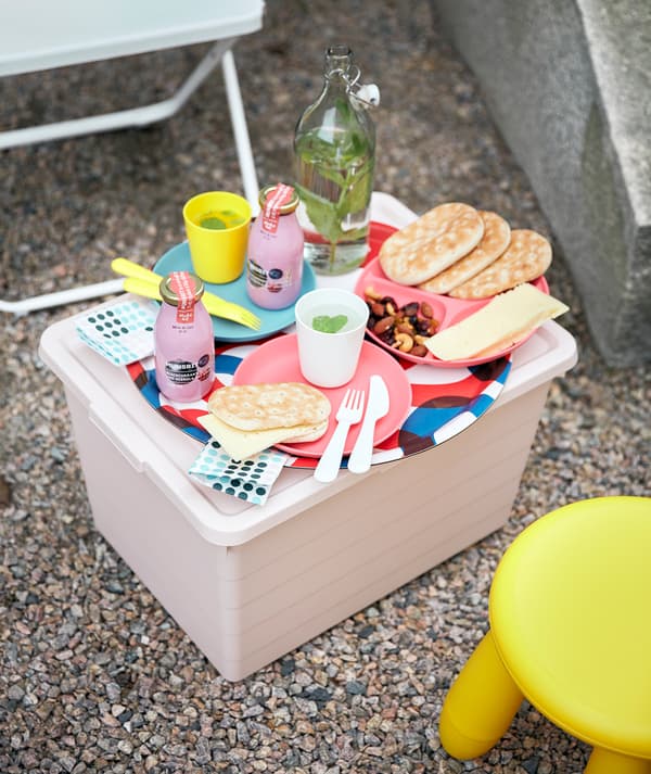 Between a FEJAN chair and a MAMMUT stool, a pink SOCKERBIT box acts as a small table set with HEROISK tableware.