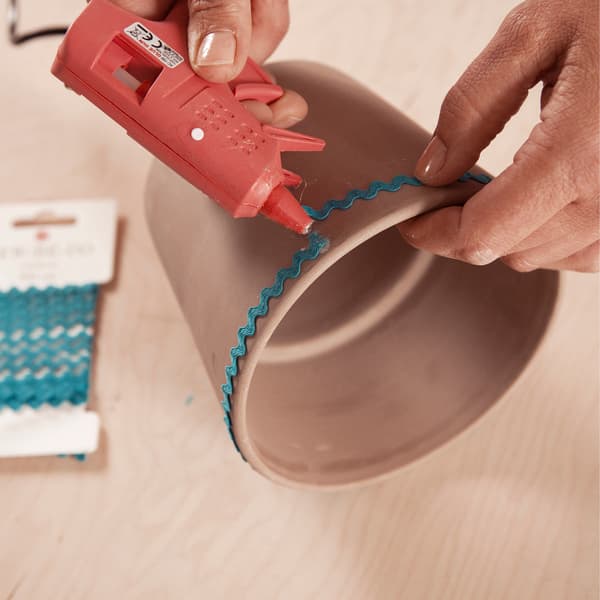 Bevestig met een lijmpistool een sierlint langs de rand van de pot.