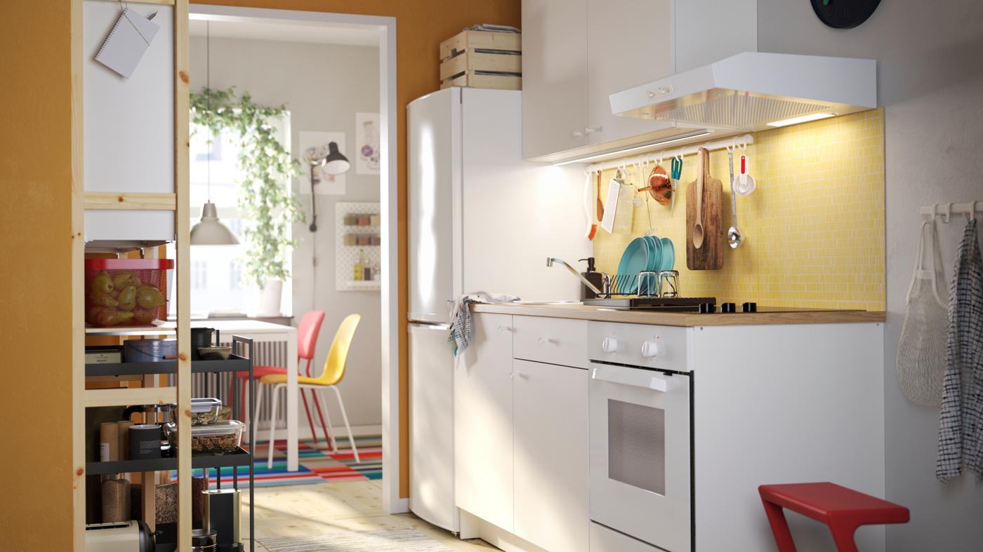 Biała kuchnia KNOXHULT, czerwony taboret ze schodkiem, drewniany regał z sosny, czarne wózki i kolorowe krzesła kuchenne.