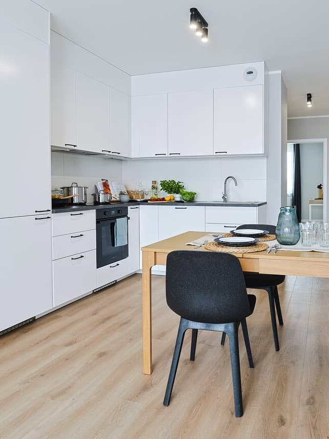 Biała kuchnia z drewnaną podłogą i dębowym stołem z czarnymi krzesłami.