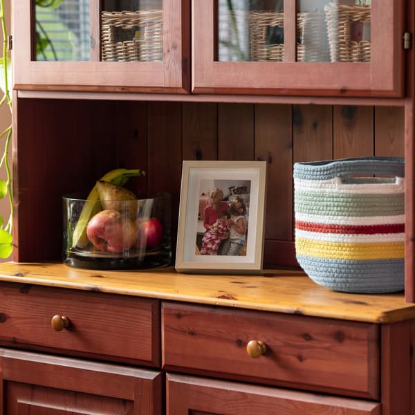 Biała ramka ze zdjęćiem RIBBA i tekstylny pojemnik stojące na drewnianym kredensie.