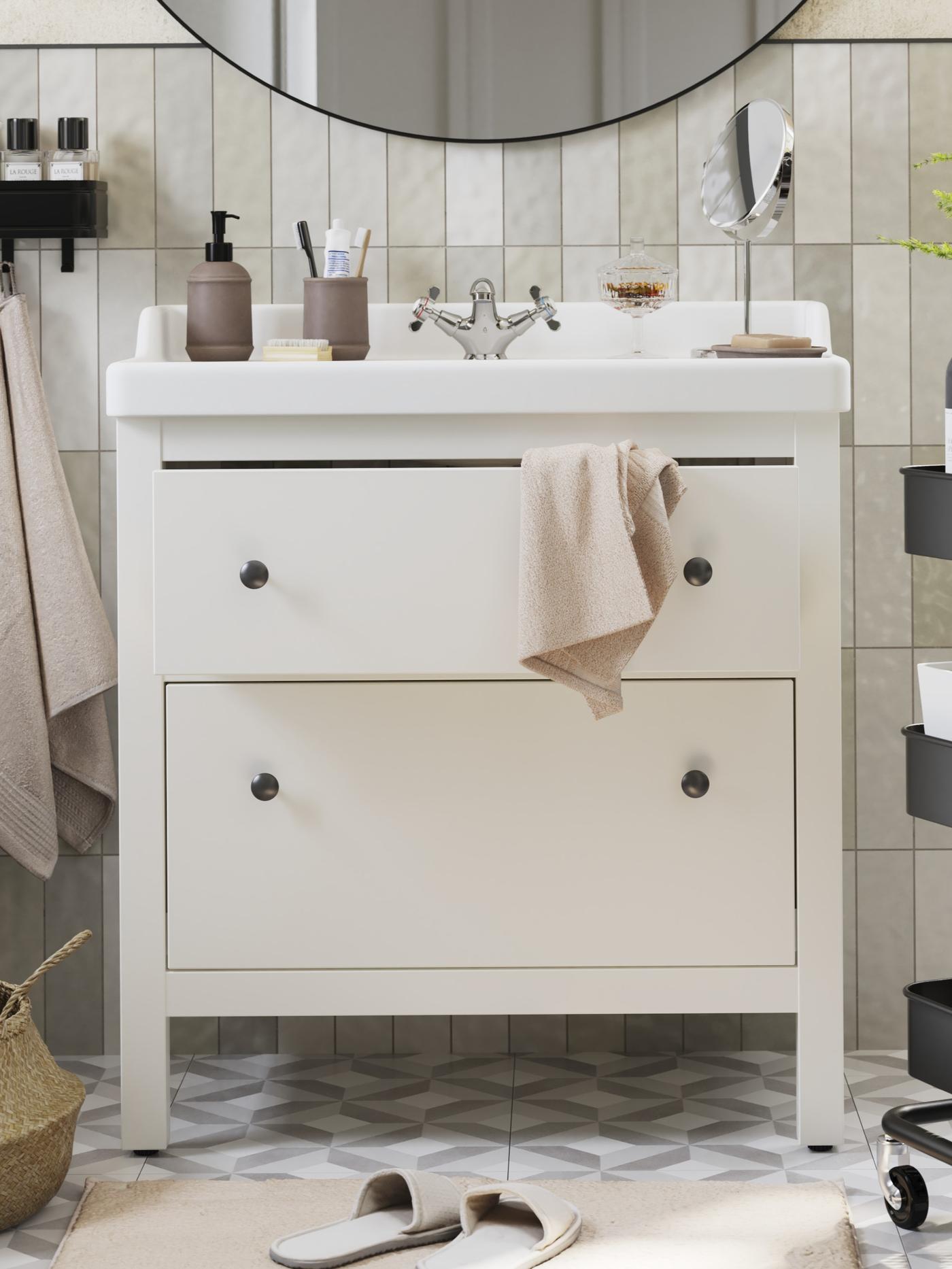 Biała szafka łazienkowa HEMNES z dwiema szufladami stoi pod okrągłym lustrem.