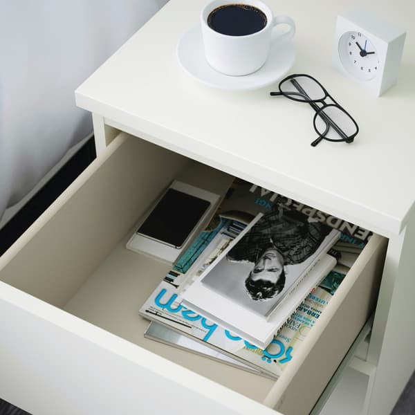 Biała szafka nocna z otwartą szufladą MALM. Na szafce stoi filiżanka kawy i okulary.