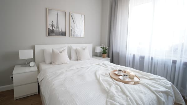 Białe łóżko i szafki nocne z serii MALM stojące w jasnoszarej sypiani przy oknie.