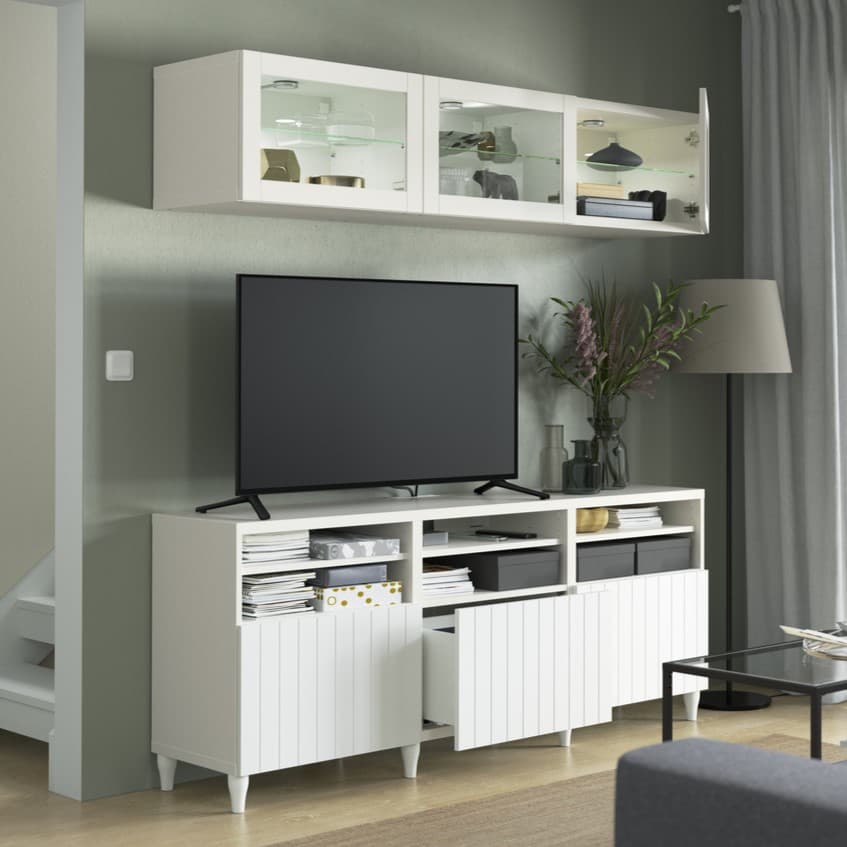 Białe szafka TV BESTÅ, na której stoi czarny telewizor. Nad telewizorem wisi rząd szafek wiszących BESTÅ.